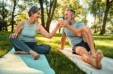 Water balance during activity. Caucasian family of two smiling to each other while sitting on yoga...