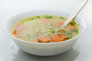 Homemade chicken soup with noodles and vegetables in a white bowl, white background. Healthy warm comfortable food.