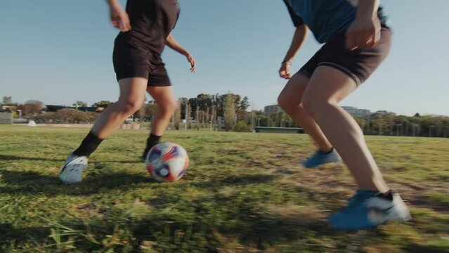 Two young female athletes playing soccer on an outdoor field on summer day, running and dribbling a ball during a game. Handheld camera, close-up shot