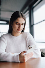 Woman in white clothes using smartphone sitting in cafe