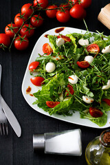 Fresh salad with cherry tomatoes, mozzarella cheese and arugula. wooden on a black background. 
