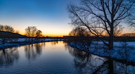 Winter panorama in Sauerland at Ruhr river near Iserlohn and Schwerte. Colorful twilight on a cold evening with blue sky and moon. Seasons greetings atmosphere in idyllic rural landscape in Germany.