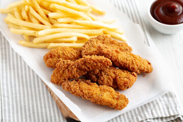Homemade Chicken Tenders with French Fries and BBQ Sauce on a rustic wooden board, side view.