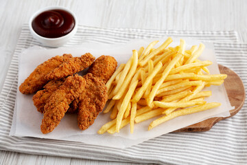 Homemade Chicken Tenders with French Fries and BBQ Sauce on a rustic wooden board, side view.