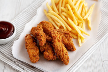 Homemade Chicken Tenders with French Fries and BBQ Sauce on a rustic wooden board, side view.
