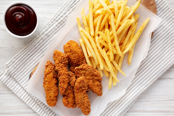 Homemade Chicken Tenders with French Fries and BBQ Sauce on a rustic wooden board, top view.