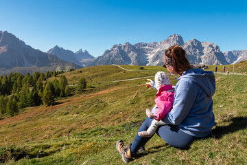 Naklejka na ściany i meble Loving mother holding baby on alpine meadow with scenic view of Sextner Rotwand, Sexten Dolomites, South Tyrol. Idyllic landscape on Klammbachalm (Malga Klammbach), Italian Alps. Tranquil atmosphere