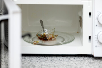 A white microwave oven with an open door. A burst bowl with a steel spoon inside the microwave