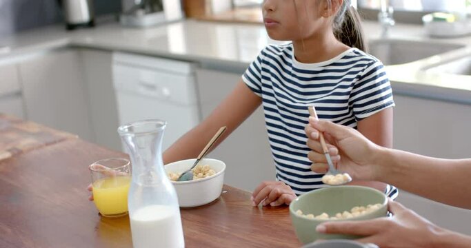 Biracial mother and daughter eating breakfast cereal in sunny kitchen, slow motion