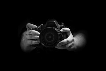 Close em mãos segurando uma câmera com fundo preto. Imagem em preto e branco.