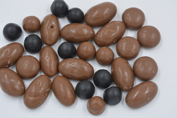 Chocolates of different sizes, peanuts, nuts, raisins are covered with milk chocolate and dark chocolate glaze, pebbles arranged on a white background.