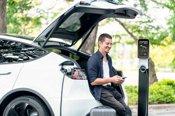 Man using smartphone online banking application to pay for electric car battery charging from EV...