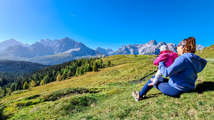 Loving mother holding baby on alpine meadow with scenic view of Sextner Rotwand, Sexten Dolomites, South Tyrol. Idyllic landscape on Klammbachalm (Malga Klammbach), Italian Alps. Tranquil atmosphere