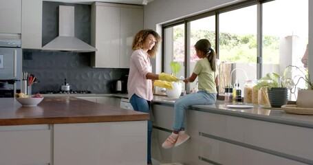 Biracial mother and daughter washing and drying dishes in kitchen, copy space, slow motion