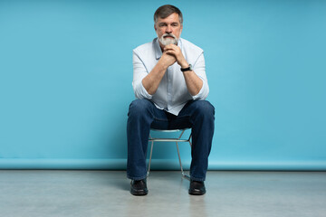 Portrait of a casual senior sitting on a chair on blue background