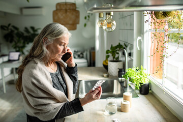 Senior woman consulting about medication over the phone in kitchen