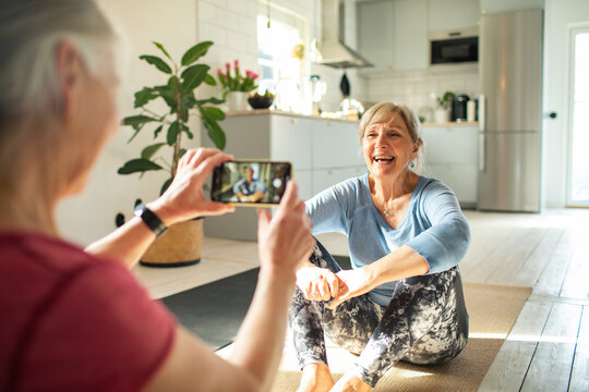 Two senior women taking pictures during home yoga session