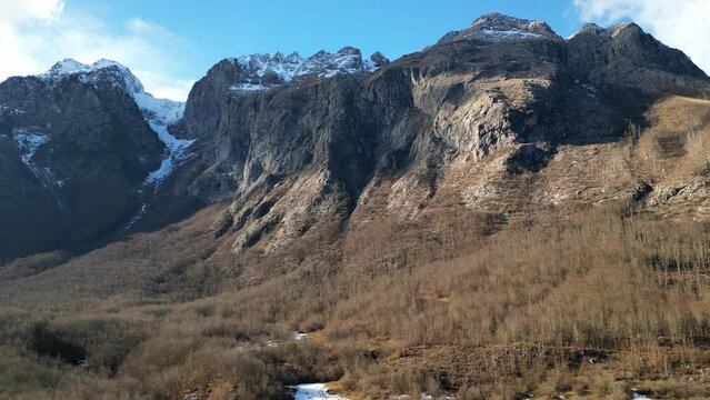 The drone flies up to a huge, relief mountain with a snow-capped peak