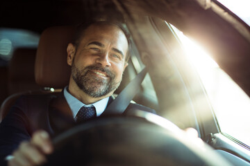 Smiling businessman driving car during sunny day