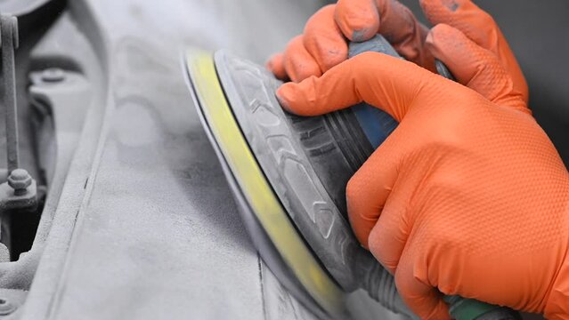 A mechanic sands the putty on a car body with a machine. Repair after an accident. 