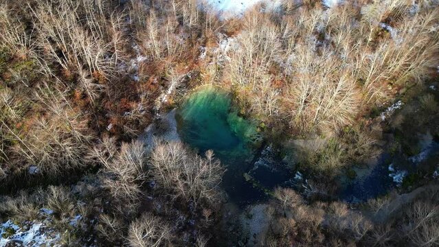 The drone flies around a small, turquoise, clear lake