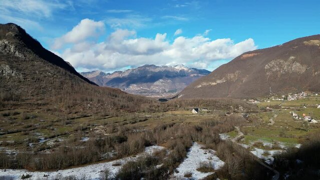 A drone flies over a snow-covered valley with trees, large mountains around