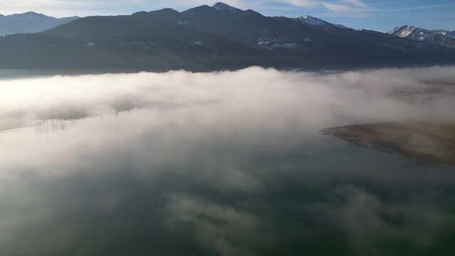 A drone flies over a mountain lake covered in thick morning fog