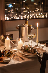 holidays, dinner party and celebration concept - close up of festive table serving for two with champagne bottle in ice bucket and candles burning at home on valentine's day