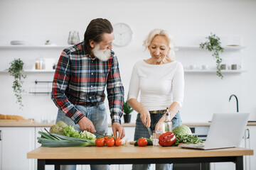 Caucasian old married man and wife prepare healthy salad, cutting thin slices of green vegetables...
