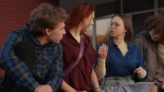 Happy friends sitting on the parapet near the school