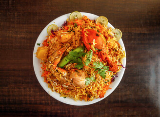 Spicy chicken biryani with potato and lemon slice served in plate isolated wooden background top view indian spices and pakistani food
