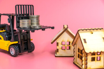 A forklift truck holds a model of a house on a pink background on a platform. The concept of buying...