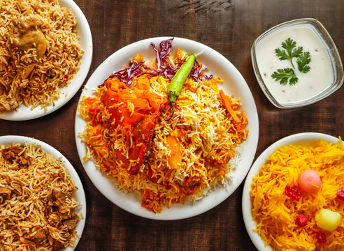 Assorted biryani, pulao with beef, chicken and zarda color ful rice served in plate isolated wooden background top view indian sweet and pakistani dessert food