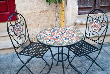 A beautiful table and two chairs decorated with red and blue mosaics in an old street