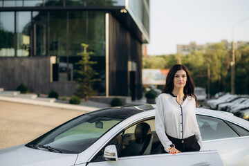Professional female manager with tablet standing near car at office building