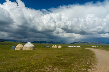 Nomadic yurt encampment sprawls across Son-Kul's grassy terrain, azure skies, distant peaks...