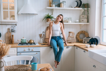 Contemplative woman sitting on a kitchen counter in a rustic setting, portraying casual home life