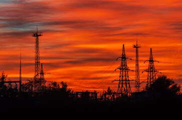 Electricity pylons silhouetted against the backdrop of a fiery sunset sky.