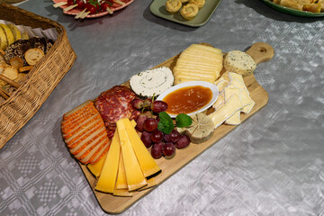 Assortment of cheeses, cured meats, grapes, and pumpkin jam on a wooden cutting board at a festive gathering.