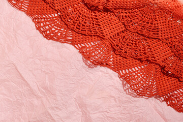 Pastel pink thin crumpled paper, creative copy background, red crocheted lace decoration.
