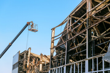 Auto crane cradle for workers and destroyed by fire industrial building. Dismantling works.
