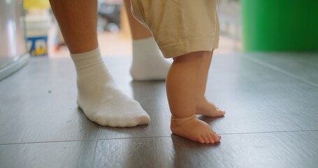 Closeup father teaches baby to walk and take first steps, father holds and supports the child and...