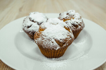 Three baked cupcakes sprinkled with powdered sugar on a white plate.