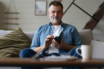 Happy smiling senior man using smartphone device while sitting on sofa at home