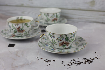 Tea set with a pattern of flowers with tea leaves scattered on a white table. Preparing a hot drink for guests