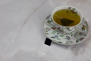 Obraz na płótnie Canvas White porcelain cup on a saucer with a brewing green tea bag on a white marble table