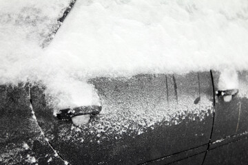 Snow covers the windows and door handles of a car during a winter storm.