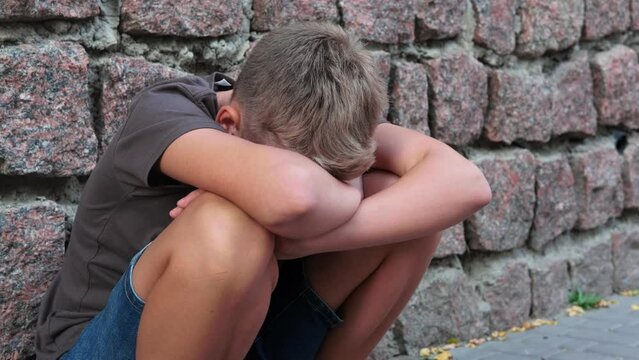 Sad depressed teenage boy alone near stone wall outside, feeling angry and lonely