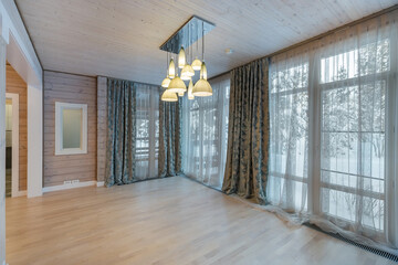 An empty room decorated with light wood in a private house. Panoramic windows with beautiful curtains.