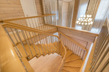 Obraz premium View of the stairs inside the living room of a private house with light wood trim. Large .windows with curtains.